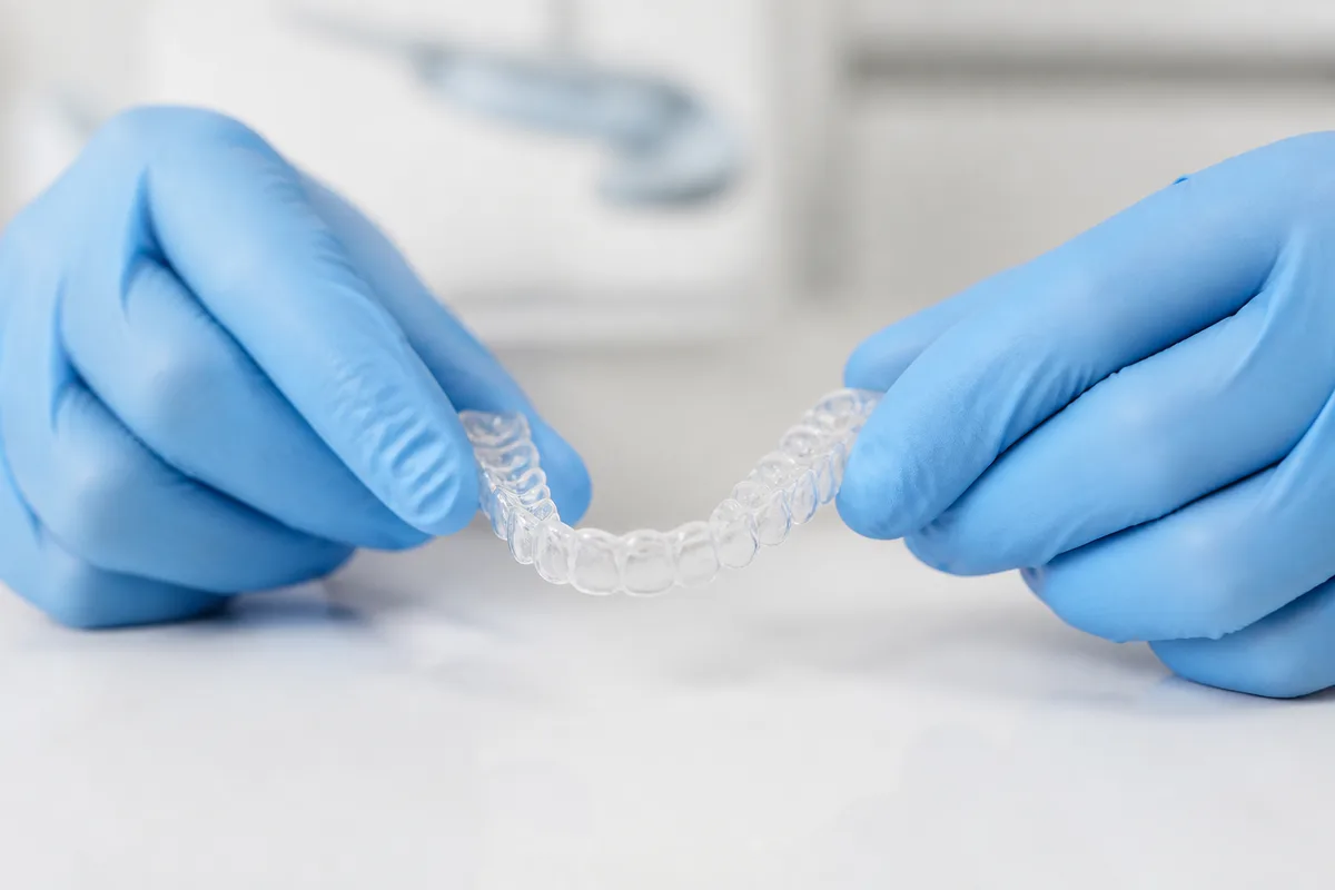 Mains gantées tenant une gouttière dentaire transparente en laboratoire